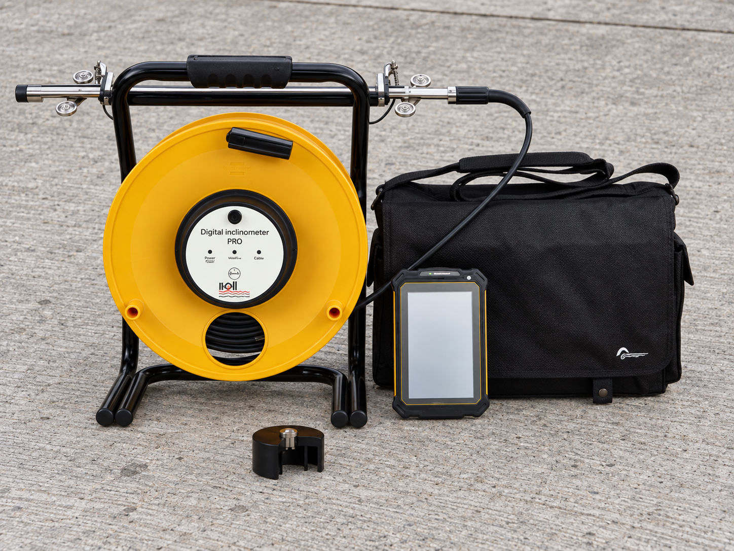 Inclinometer probe, yellow cable reel, handheld readout and carrying bag on concrete pavement