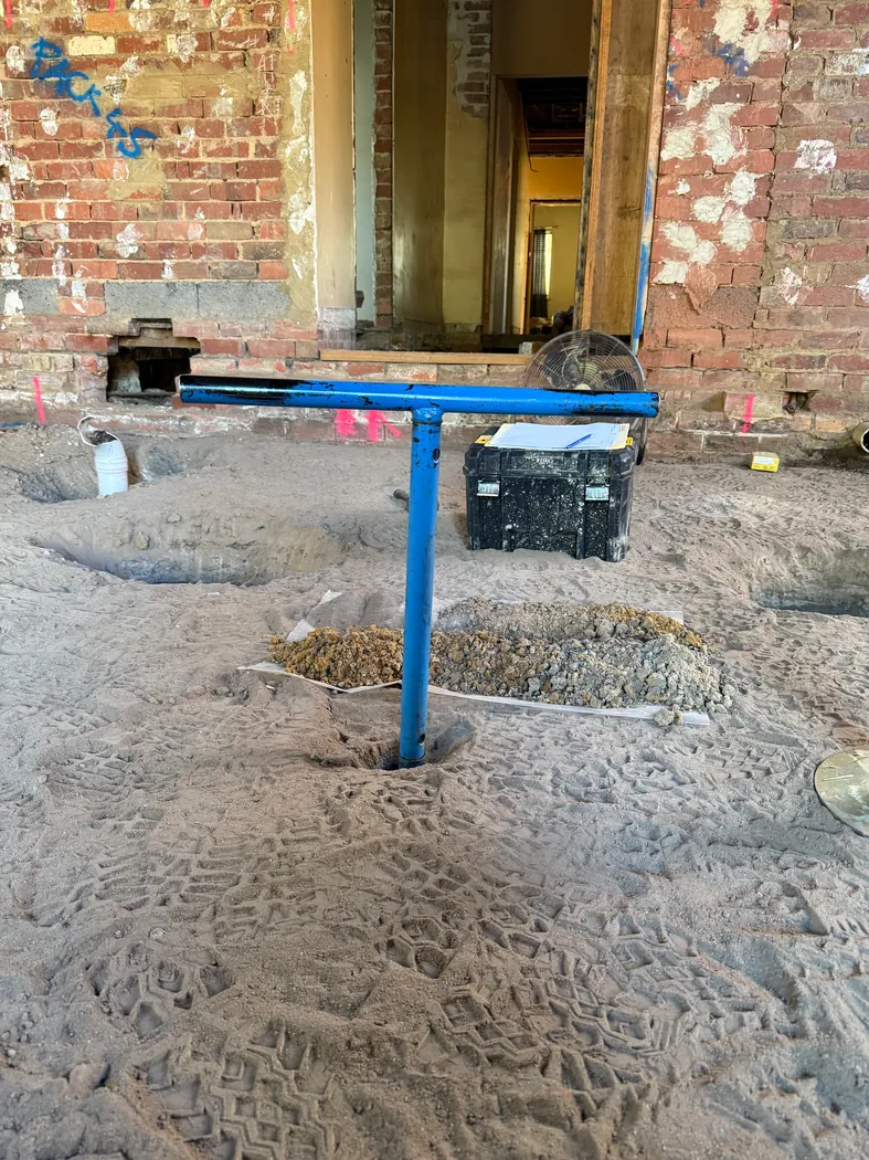 Hand-auger investigation beside a brick building under renovation