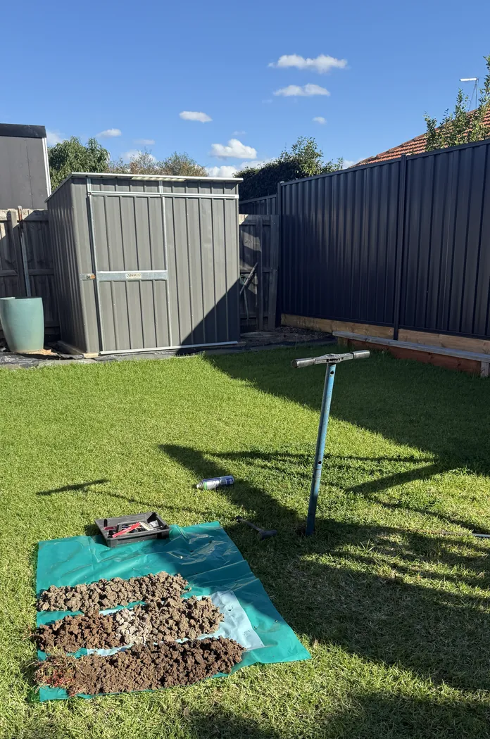 Hand-auger investigation in a backyard beside a garden shed