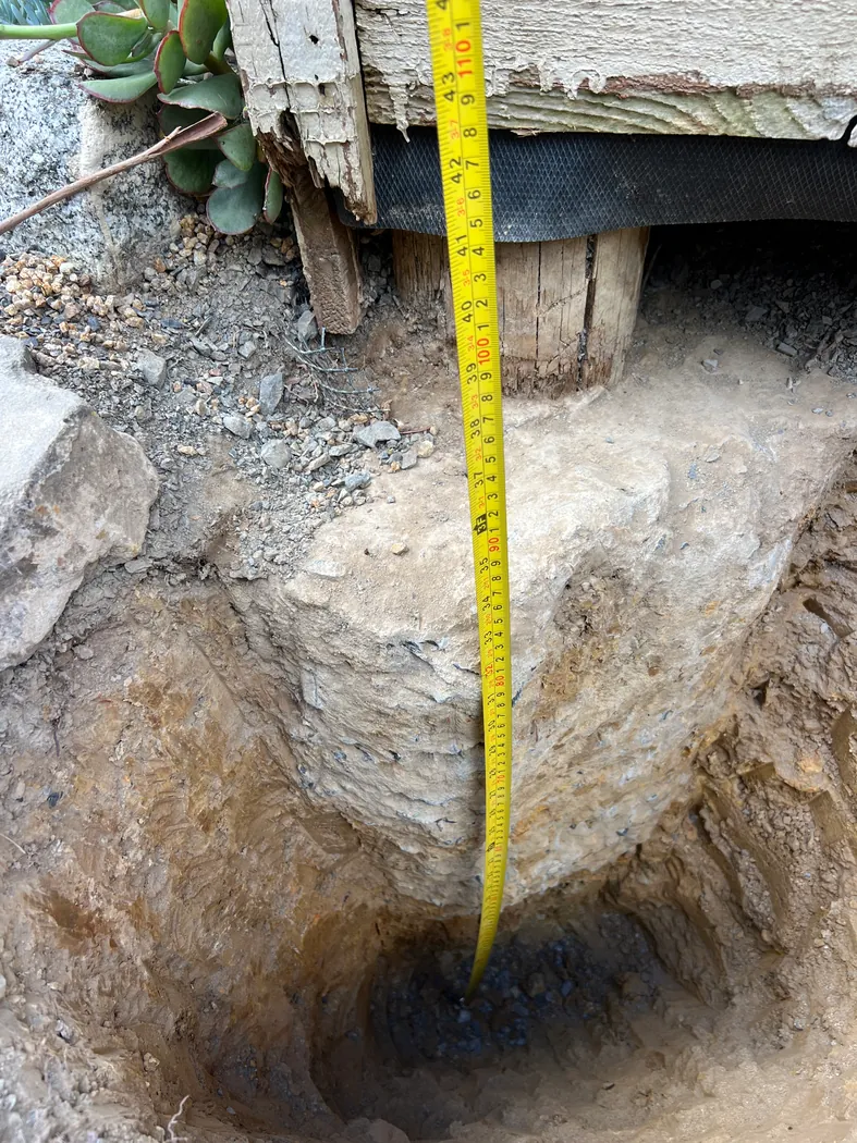 Inspection excavation beside an existing structure with a tape measuring depth