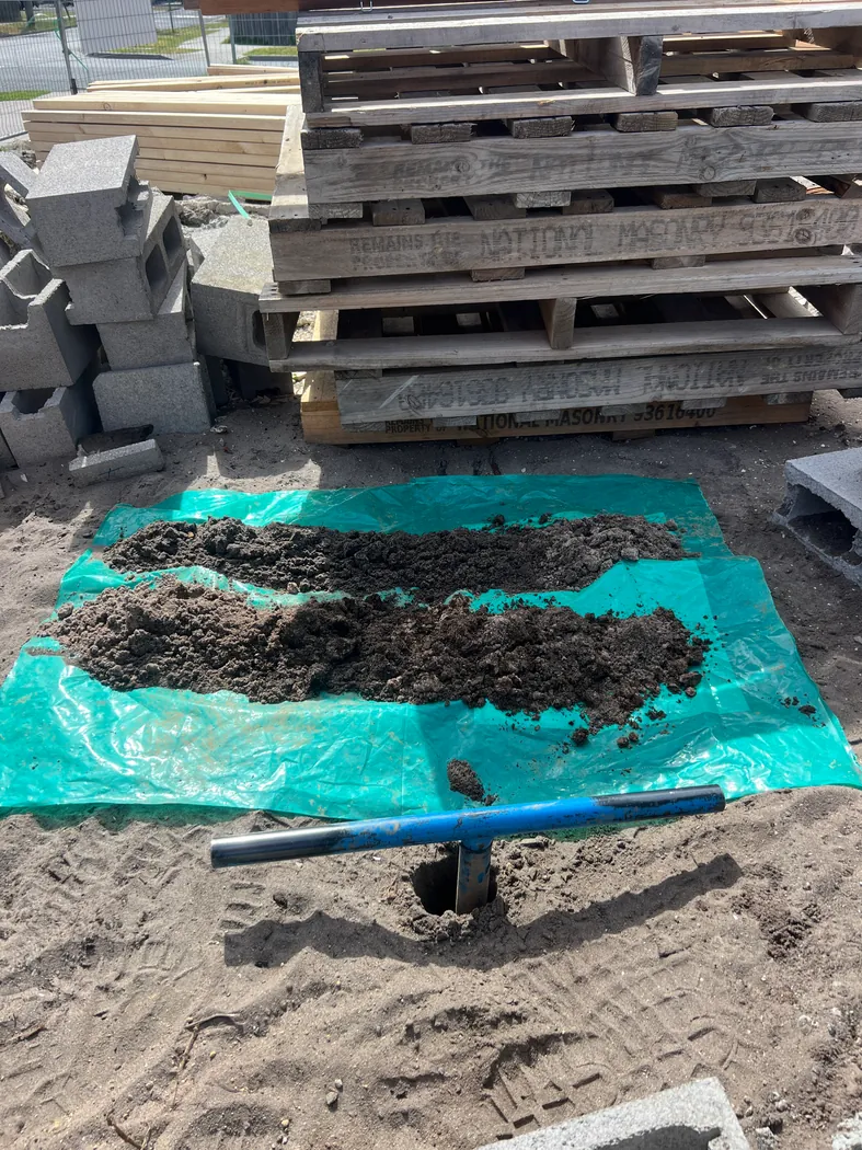 Hand auger and soil samples in a work area beside stacked pallets