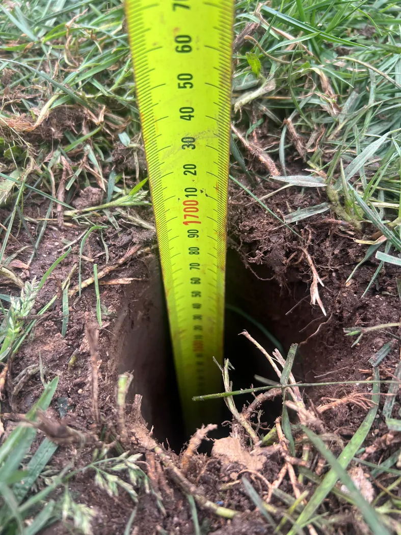 Measuring tape in a soil investigation hole through grass-covered ground