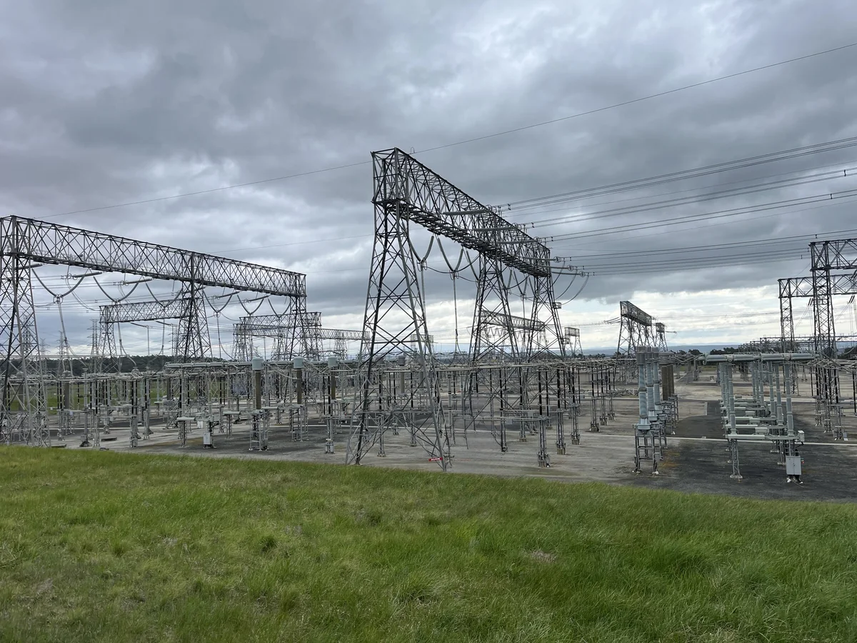 Steel gantries, overhead conductors and electrical equipment at Hazelwood Terminal Station, viewed from a grassy embankment.