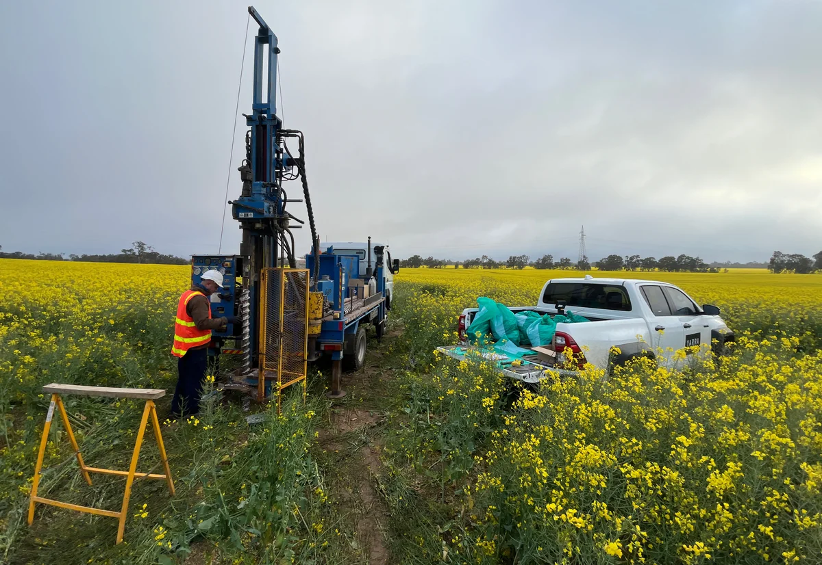 Drilling rig and field crew beside a Yarra Geotechnics vehicle carrying sample bags in a flowering canola field at Joel Joel.