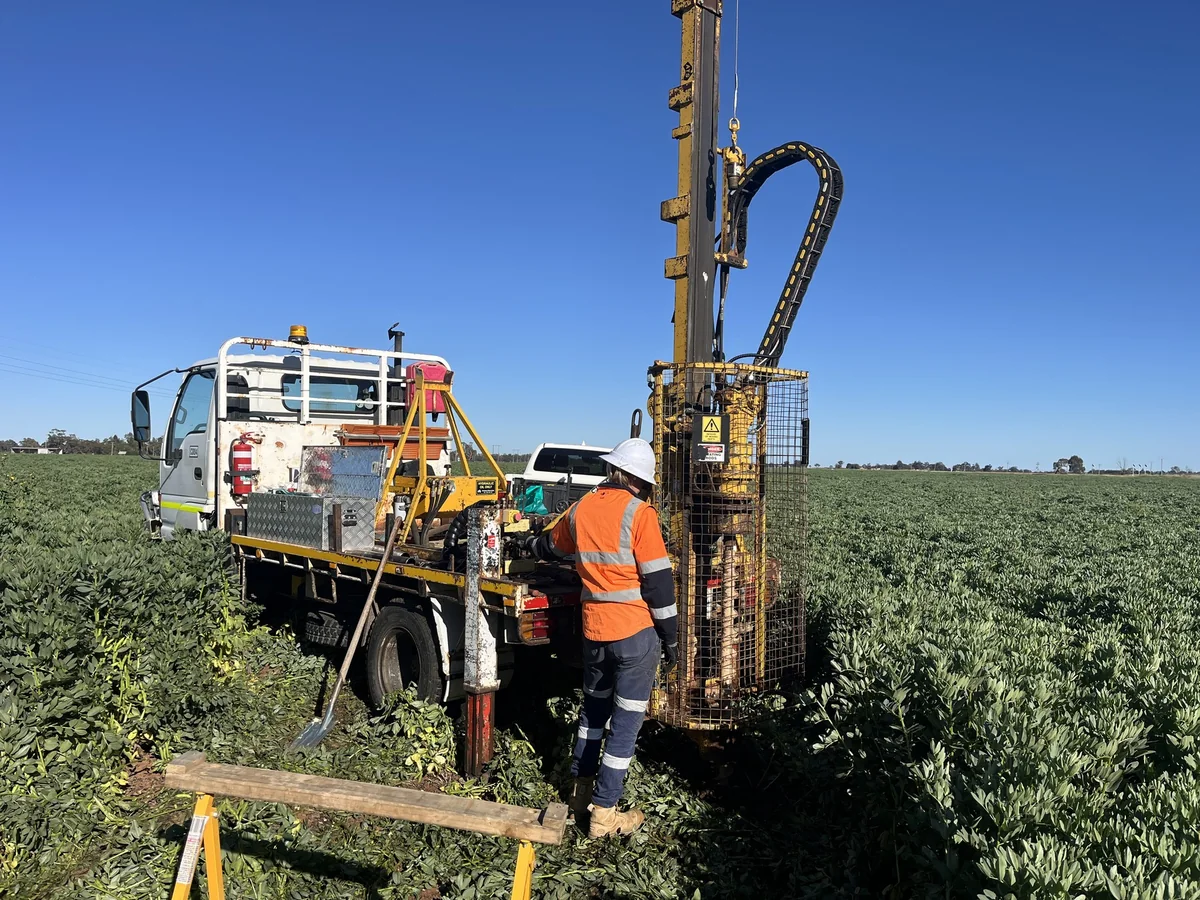Truck-mounted drill rig working in an open agricultural landscape.