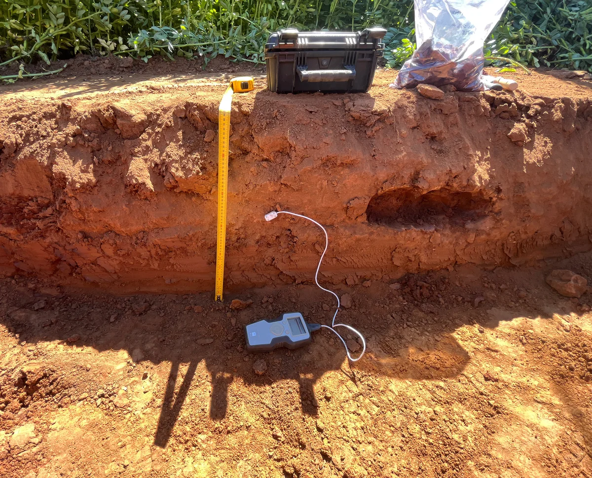 Thermal testing probe and meter beside a measuring tape in an exposed red-soil test pit at Yanco.